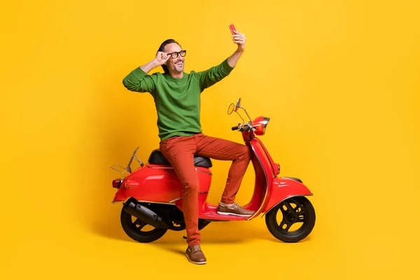 Zdjęcie faceta trzymać smartfon jeździć motorower podjąć selfie nosić specyfikacje zielony sweter spodnie buty odizolowany żółty kolor tło — Zdjęcie stockowe