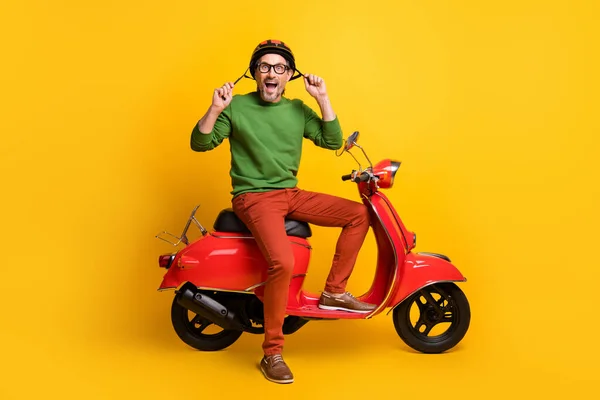 Foto de tipo loco en scooter boca abierta desgaste casco especificaciones pantalones suéter verde aislado color amarillo fondo —  Fotos de Stock