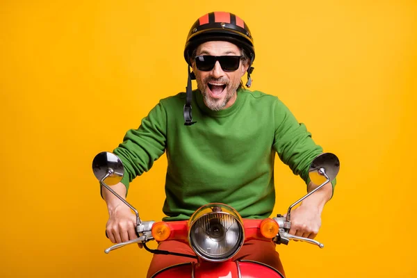 Zdjęcie niesamowite śmieszne facet jeździć motorower nosić okulary kask zielony pullover odizolowany żółty kolor tło — Zdjęcie stockowe