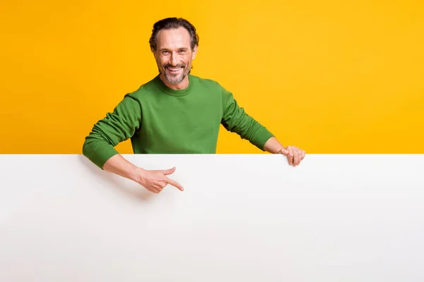 Photo of promoter man hold white placard direct finger empty space wear green sweater isolated yellow color background — Stock Photo, Image