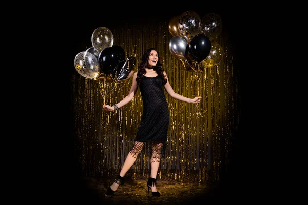 Foto von charmant beeindruckt junge Frau gekleidet schwarzes Outfit mit Luftballons isoliert Goldglanz Hintergrund — Stockfoto