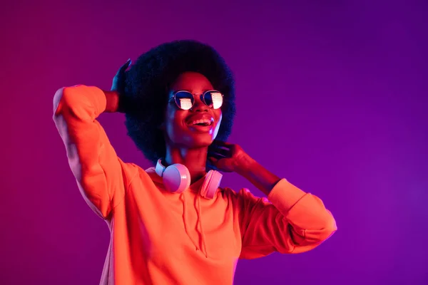 Fénykép a gondtalan lány touch frizura néz ki üres tér kopás kapucnis fejhallgató napszemüveg elszigetelt gradiens neon háttér — Stock Fotó