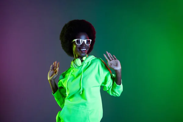 Fotografie veselá dáma tanec těšit nosit sluchátka brýle mikina izolované gradient zelený neon pozadí — Stock fotografie