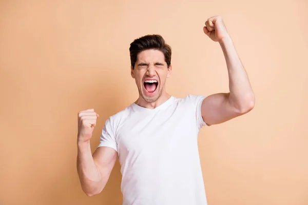 Foto van vrolijke jongeman gesloten ogen heffen vuisten vieren overwinning geïsoleerd op pastel beige kleur achtergrond — Stockfoto