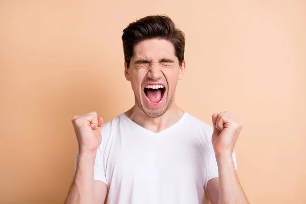 Retrato de hooray morena hombre gritar manos puños llevar camiseta blanca aislada sobre fondo de color beige — Foto de Stock