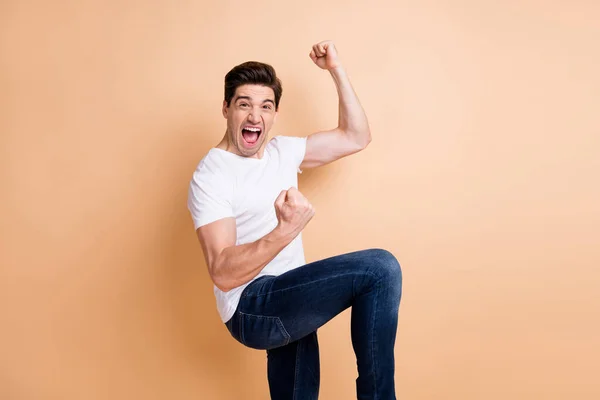 Profiel side photo of crazy happy young guy raise fists kampioen slijtage jeans geïsoleerd op beige kleur achtergrond — Stockfoto