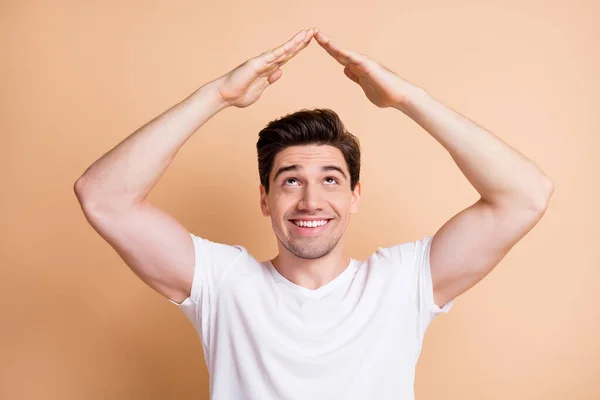 Bilde av munter fyr som slår opp tomme romarmer viser hus-form toothy smil isolert på beige fargebakgrunn – stockfoto