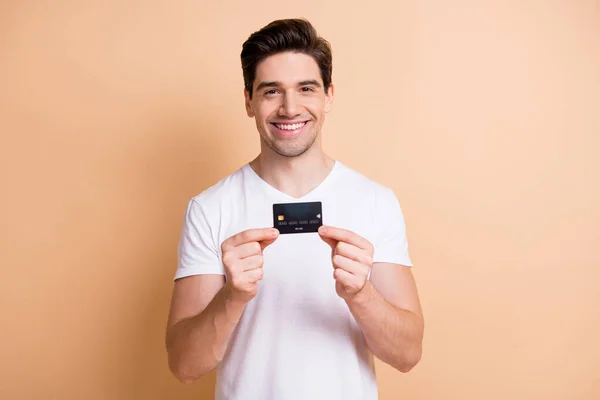 Retrato de satisfeito jovem sorriso mãos segurando cartão bancário isolado no fundo cor bege — Fotografia de Stock