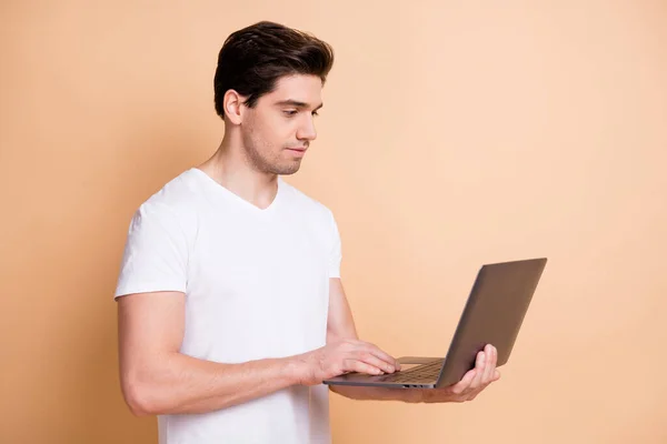 Profil portret optymistyczny brunet człowiek typ laptop nosić biały t-shirt izolowany na beżowym tle koloru — Zdjęcie stockowe