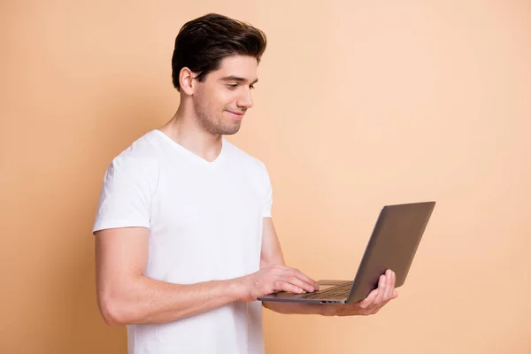 Foto de chico joven positivo mantenga uso netbook escribir mensaje mirar pantalla aislada sobre fondo de color beige —  Fotos de Stock