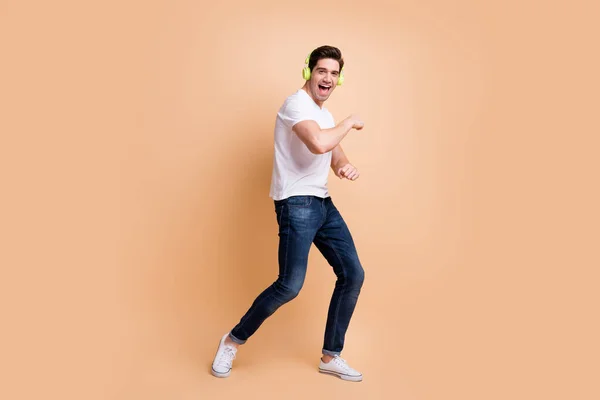 Pełny rozmiar zdjęcie optymistyczne brunet człowiek taniec nosić biały t-shirt dżinsy trampki izolowane na beżowym tle kolor — Zdjęcie stockowe