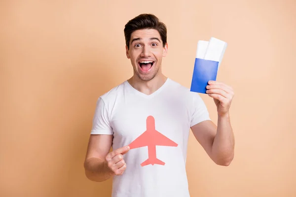 Zdjęcie optymistycznego brunet man stand hold bilety lotnicze nosić biały t-shirt izolowany na beżowym tle — Zdjęcie stockowe