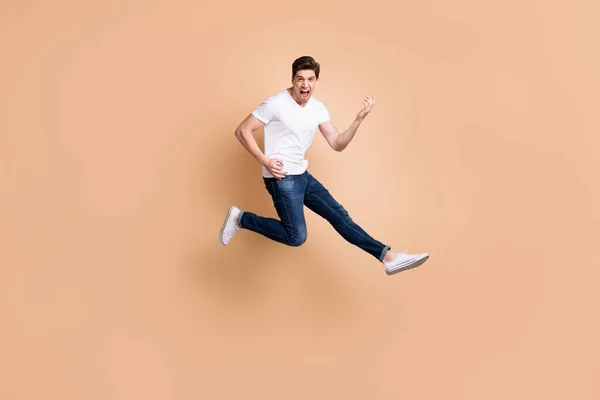 Full Size Profilfoto von Hurra Brunet Mann springen spielen Gitarre schreien tragen T-Shirt Jeans Turnschuhe isoliert auf beige Hintergrund — Stockfoto