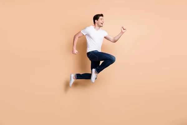 Taille réelle photo de profil de hourra brunet homme saut courir porter t-shirt jeans baskets isolées sur fond de couleur beige — Photo