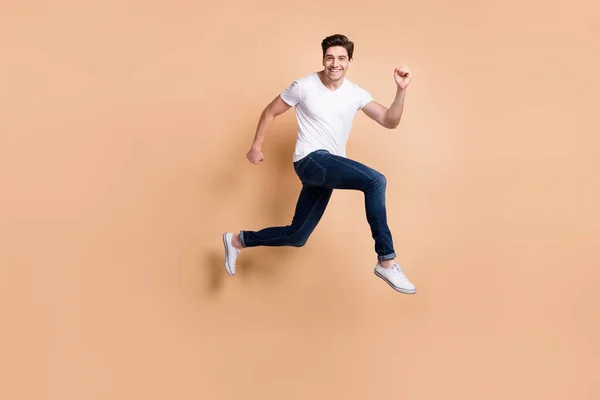 Full storlek profil foto av hurra brunett man hoppa springa slitage t-shirt jeans sneakers isolerad på beige bakgrund — Stockfoto