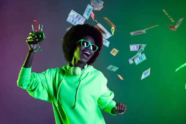Zdjecie 90s styl wesoły lady trzymać szklanego alkoholu dolary upadek nosić sunglass bluza odizolowany gradient zielony neon tło — Zdjęcie stockowe