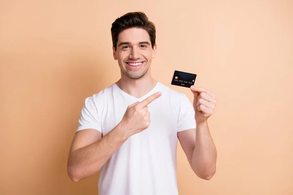 Portret van knappe positieve vrolijke persoon geven vinger debetkaart geïsoleerd op beige kleur achtergrond — Stockfoto