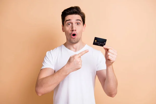 Portret van onder de indruk brunet man point card dragen witte t-shirt geïsoleerd op beige kleur achtergrond — Stockfoto