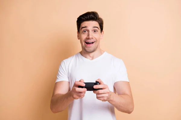 Portrait of impressed brunet man playstation wear white t-shirt isolated on beige color background — Stock Photo, Image