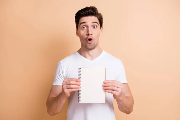 Портрет враженого брюнетки чоловік показує блокнот у білій футболці ізольовані на бежевому кольоровому фоні — стокове фото