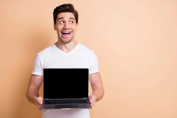 Retrato de pessoa alegre olhar espaço vazio boca aberta segurar laptop mostrando exibição isolada no fundo cor bege — Fotografia de Stock