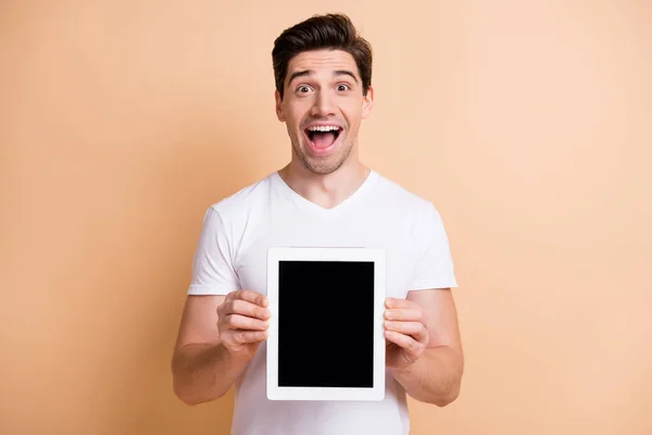 Profil portret pod wrażeniem brunet man show tablet nosić biały t-shirt izolowany na beżowym tle — Zdjęcie stockowe
