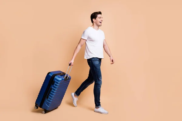 Фотографія профілю враженого брюнетки чоловік йде тримати сумку одягати футболки джинси кросівки ізольовані на бежевому фоні — стокове фото