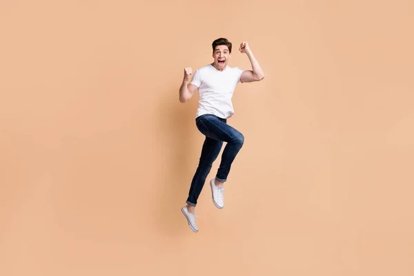 전체 크기 프로필 사진 호 레이 브루 넷 남자 점프 베지 배경에 분리 된 티셔츠 청바지 스니커즈를 착용 — 스톡 사진