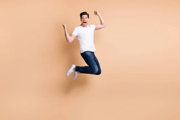 Full storlek profil foto av hurra brunett man hoppa skrika slitage t-shirt jeans sneakers isolerade på beige bakgrund — Stockfoto