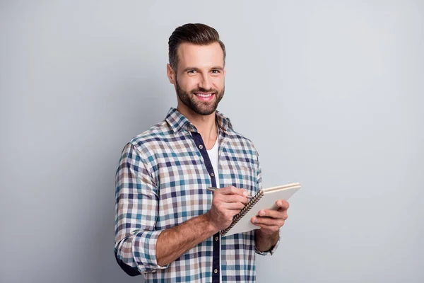 Foto retrato de un joven trabajador escribiendo notas en billetes de bloque sonriendo en camisa a cuadros aislada sobre fondo de color gris — Foto de Stock