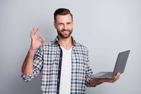 Портрет привлекательного веселого парня, держащегося за руки с помощью ноутбука, показывающего хорошо знакомое объявление, изолированное на сером пастельном фоне — стоковое фото