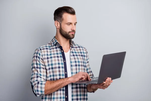 Porträtt av attraktiva skickliga fokuserad skäggig kille som håller i handen med hjälp av laptop skriva e-post isolerad över grå pastell färg bakgrund — Stockfoto