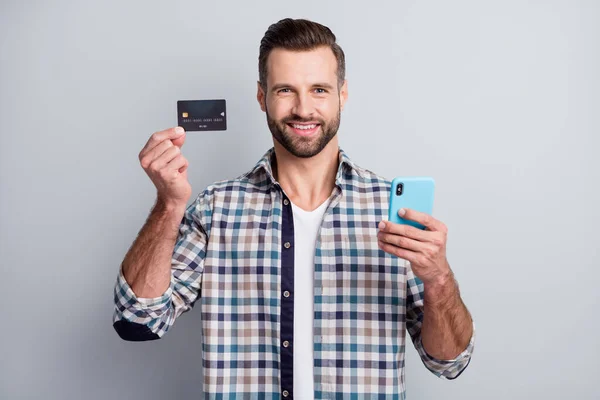 Foto portret van vrolijke man houden mobiele telefoon tonen bank credit card geïsoleerd op grijze achtergrond — Stockfoto