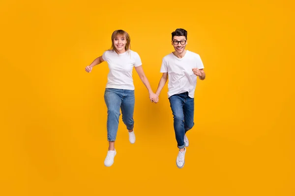 Teljes hosszúságú fotó vicces édes két személy öltözött fehér póló fut ugrás gazdaság karok elszigetelt sárga szín háttér — Stock Fotó