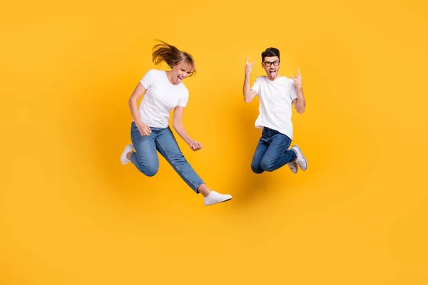 Teljes hosszúságú fotó kemény hűvös fiatal pár viselni fehér póló jumping mutatja hard rock jel gitáros elszigetelt sárga háttér — Stock Fotó