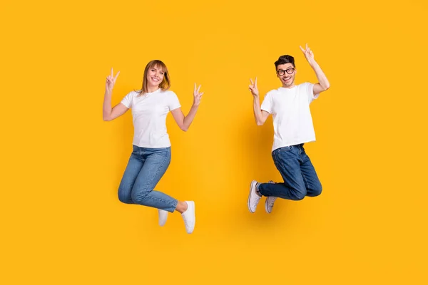 Ganzes Foto von süßen hübschen zwei Personen gekleidet weißes T-Shirt springen hoch zeigt V-Zeichen isoliert gelben Farbhintergrund — Stockfoto