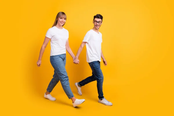 Full längd foto av charmiga söta par bära vit t-shirt glasögon som håller händerna gående isolerad gul färg bakgrund — Stockfoto
