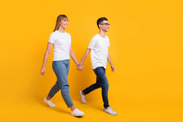 Full längd foto av ganska bedårande personer klädd t-shirt promenader hålla händerna tomma utrymme isolerad gul färg bakgrund — Stockfoto