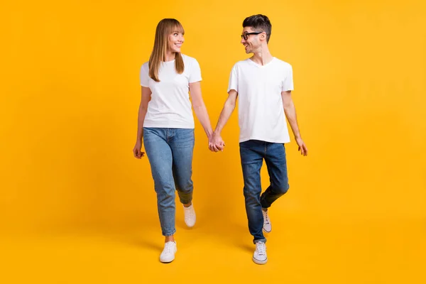 Full längd foto av söta charmiga par slitage t-shirt glasögon hålla händerna ser varandra isolerad gul färg bakgrund — Stockfoto
