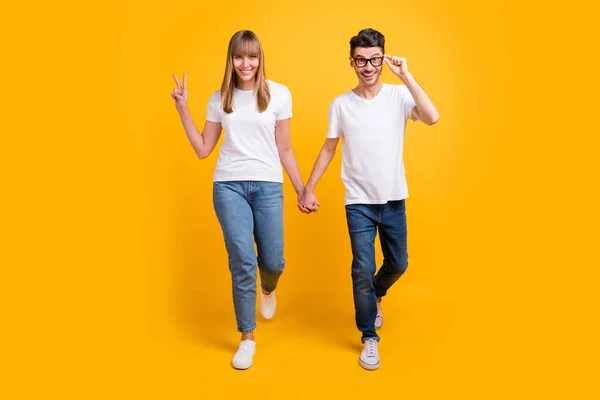 Teljes hosszúságú fotó vicces édes fiatal pár viselni fehér póló szemüveg fogja a kezét karok v-jel izolált sárga háttér — Stock Fotó