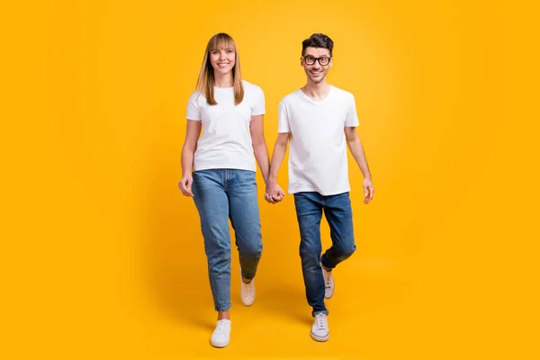 Full längd foto av funky söt två personer klädd vit t-shirt promenader hålla händerna isolerade gul färg bakgrund — Stockfoto