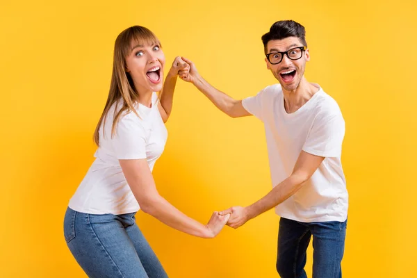 Foto de casal muito animado jovem desgaste branco t-shirt óculos segurando as mãos braços dançando isolado cor amarela fundo — Fotografia de Stock