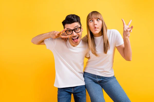 Photo of charming pretty young couple wear white t-shirt spectacles dancing showing v-signs isolated yellow color background — Stock Photo, Image
