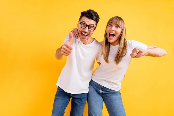 Foto de dulce encantadora pareja joven usar gafas de camiseta blanca bailando mostrando el pulgar hacia arriba aislado color amarillo fondo —  Fotos de Stock