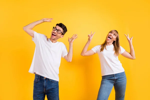 Foto de engraçado encantador duas pessoas vestidas branco t-shirt óculos mostrando v-sinais dançando isolado cor amarela fundo — Fotografia de Stock