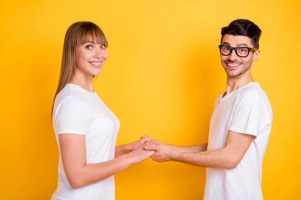 Foto de muito bonito jovem casal desgaste branco t-shirt óculos segurando as mãos braços isolado cor amarela fundo — Fotografia de Stock