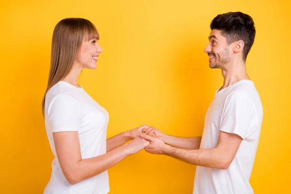 Foto av glada söta två personer klädda vit t-shirt håller händerna ser varandra isolerad gul färg bakgrund — Stockfoto