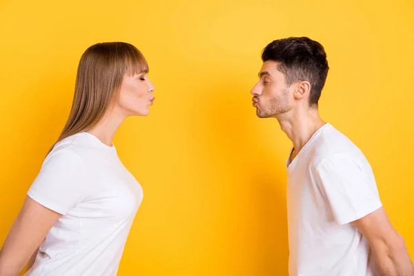 Фото чарівної мрійливої молодої пари в білій футболці готові цілувати один одного закритими очима ізольований жовтий кольоровий фон — стокове фото