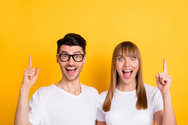 Foto de encantador animado duas pessoas vestidas branco t-shirt óculos apontando para cima espaço vazio isolado cor amarela fundo — Fotografia de Stock