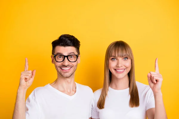Foto van schattige charmante twee personen gekleed wit t-shirt bril wijzen omhoog vingers lege ruimte geïsoleerde gele kleur achtergrond — Stockfoto